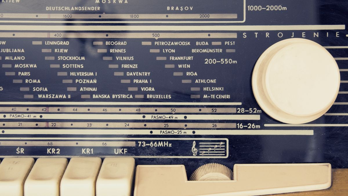 A detailed view of a vintage radio's tuning dial with city stations displayed.